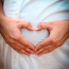 A simple and iconic maternity photo. The mother-to-be forms a heart with her hands over her baby bump, a universal symbol of the immense love she already feels for her child.