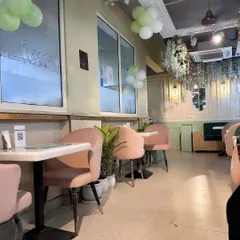 The interior of this charming cafe uses a soft color scheme of pastel pink and mint green. The design includes comfortable upholstered chairs, marble-topped tables, and decorative wall paneling for an elegant feel.