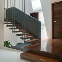 The floating staircase at "The Mantle" features solid teak wood treads. The rich grain of the wood provides a warm, natural counterpoint to the minimalist steel structure.