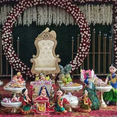 A full view of a traditional gift platter setup for a function at CR Simha Samskruthika Bhavana. The arrangement features dolls, peacock motifs, and gift platters, all set against a grand floral backdrop.
