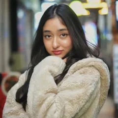 A cozy and cute portrait taken at night in a bustling market. The warm jacket and the soft glow of the background lights create a comfortable and inviting atmosphere.