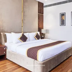 This executive hotel room features a custom upholstered headboard with metallic accents and textured wall panels. The design focuses on creating a luxurious and restful environment with dedicated task lighting and premium materials.