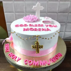 A special cake for a First Holy Communion. This elegant white and pink cake is decorated with a cross, rosary beads, and a small bible.
