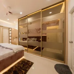 A luxurious master bedroom with floor-to-ceiling sliding wardrobes. The frosted glass doors with golden frames and under-bed lighting create a glamorous and sophisticated ambiance.