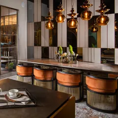 The warm, cheerful orange accents of the dining chairs create an inviting and energetic atmosphere. The reflective surfaces of the mirrored wall paneling and amber glass pendants enhance the ambient light.