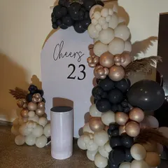 An elegant and modern "Cheers to 23" birthday setup. This features a minimalist white backdrop with a chic balloon arrangement in black, white, and rose gold.