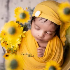 A little ray of sunshine. This newborn boy is wrapped snugly in yellow and surrounded by sunflowers, creating a bright, cheerful, and heartwarming portrait.