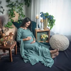 A relaxed and comfortable portrait in a beautiful sage green gown. The earthy tones of the bohemian setup, complete with wooden toys and woven cushions, create a cozy and inviting atmosphere.