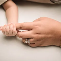 A newborn's hand holding onto mom's finger, right next to her special 'Maa' bracelet. It's a beautiful way to personalize this classic shot.