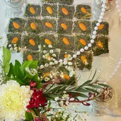 An overhead view of the pistachio mithai arrangement. Each sweet is individually wrapped for freshness and presented with care, accompanied by small silver containers and a delicate pearl string.