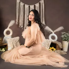 A gentle, seated pose from a boho maternity shoot. The setup includes macrame pillows, pampas grass, and soft lighting to create a comfortable and serene environment for your portraits.