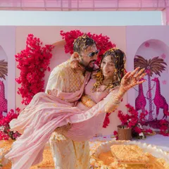 Pure, uninhibited joy at a Haldi ceremony. The groom lifts his bride, both covered in turmeric and flowers, against a backdrop of bright pink bougainvillea. This is the energy I aim to create.