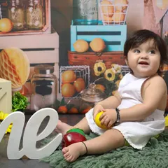 A fruity and fun first birthday. This little one is celebrating her milestone surrounded by fresh fruits and a rustic, market-themed backdrop, showing off her happy smile.