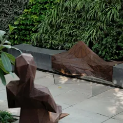 A courtyard featuring geometric, origami-inspired sculptures against a living green wall. The art pieces, created in collaboration with Formforge, add a contemporary and thought-provoking element to the quiet space.
