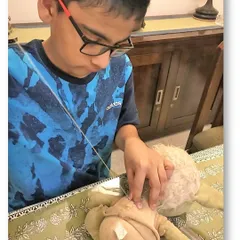 With focused concentration, a young boy stitches up his favorite toy. This activity not only teaches a practical skill but also fosters a sense of responsibility and care for one's belongings.