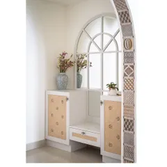 The foyer's shoe storage and seating unit, featuring a mirror that echoes the arch's shape. The design uses cane shutters and a clean white finish to create a bright and functional entryway.