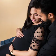 A close-up, intimate portrait of an expecting couple. The partner embraces the mom-to-be from behind as they both look down at the baby bump, capturing a tender moment in a classic maternity couple shoot.