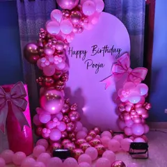 A beautiful pink-themed birthday party for Pooja. The setup includes a custom arch backdrop, an elaborate balloon garland with chrome accents, and decorative bow props.