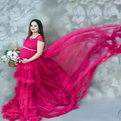 A dynamic studio shot featuring a mom-to-be in a vibrant pink ruffled gown. The "flying fabric" effect adds a touch of magic against the floral backdrop.