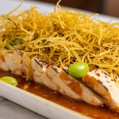 Silken tofu, but with a story of contrasts. This Tofu Carpaccio is served with a ginger ponzu dressing, avocado crema, and a pile of crispy sweet potato strings for texture. Minimal on the plate, memorable on the palate.