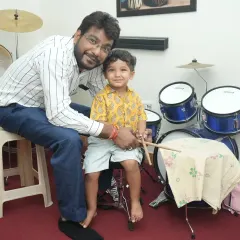 A teacher guides our youngest drum student, showing him how to hold the drumsticks. We ensure a supportive and encouraging start for children beginning their musical journey.