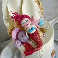 A detailed close-up of the mermaid figure shows the level of artistry involved. Her cheerful expression and the texture of her tail are crafted from sugar to bring this magical character to life.