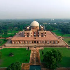 A wide aerial photograph of Humayun's Tomb, capturing the full monument and its symmetrical gardens. This shot highlights the tomb's grandeur and its peaceful setting within a lush green landscape in the heart of Delhi.