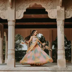 A beautiful solo portrait of the bride twirling in her multi-colored Haldi lehenga. This shot captures her happiness and the beauty of her outfit against an elegant architectural backdrop.