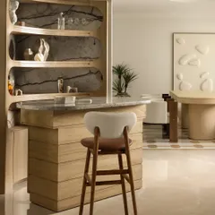 The bar is the centerpiece of Ecru Maison, crafted in warm light wood with a polished marble countertop. We designed the organically curved shelves against a dramatic marble backdrop to be both a functional hub and a sculptural feature.