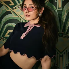 A playful and retro-inspired shoot with Dhvani Bhanushali. The scalloped polo crop-top from Lovebirds Studio, paired with pink-tinted glasses, creates a fun and stylish vibe against the art-deco wallpaper.
