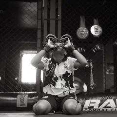 A young fighter kneels inside the cage, a moment of quiet focus before the storm. This black and white shot captures his determination.