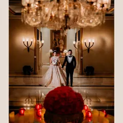 A grand, romantic portrait of the couple, framed by a crystal chandelier and a stunning floral centerpiece. The warm lighting and opulent surroundings of the palace hotel create a truly luxurious and cinematic feel.