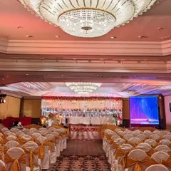 A wide view of the ballroom, showing the grand stage with its intricate white and red floral backdrop, ready to welcome guests for the wedding ceremony.