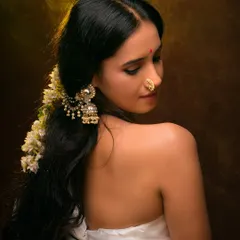 A classic ethnic portrait with a focus on traditional jewelry. The warm lighting and rich brown background create a painterly effect, emphasizing the model's serene beauty.