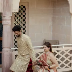 A candid moment of the couple walking hand-in-hand through the corridors of the palace venue. Their traditional outfits and the beautiful architecture create a royal feel.