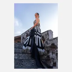 A powerful low-angle shot of a model on a decorated staircase, wearing a modern black and white lehenga. This perspective accentuates the dramatic flow of the skirt and creates a strong, statuesque silhouette.