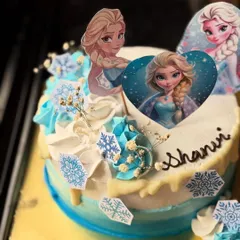 A magical Disney Frozen themed cake for a 9-year-old princess. It features Elsa and Anna toppers, snowflake decorations, and a blue and white ombre effect.