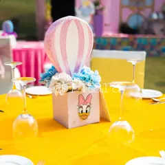 A close-up of a table centerpiece featuring a Daisy Duck-themed box with a miniature hot air balloon. These small, thoughtful details are what make a themed party truly special.