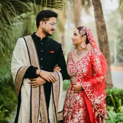 A classic portrait of a bride and groom, where her vibrant red lehenga stands out against the lush greenery. The way they look at each other speaks volumes about their love story.