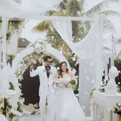 A fairytale entrance for a modern couple. They walk through a beautiful white archway, showered with bubbles, creating a magical and joyous moment at their daytime gala.