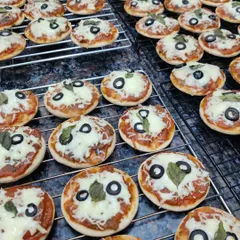 A batch of our mini pizzas fresh out of the oven. These bite-sized treats are perfect for parties, topped with our homemade tomato sauce, mozzarella cheese, basil, and a black olive.