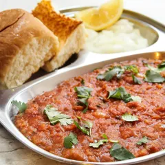 A close up of our authentic Pav Bhaji, served in a traditional steel plate with buttered pav, chopped onions, and a lemon wedge. It’s a taste of Mumbai street food delivered to your home.