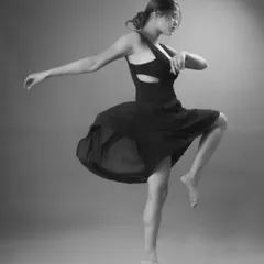 A graceful and athletic pose frozen in time. The monochrome treatment emphasizes the muscular definition and the beautiful shape created by the dancer and her dress, showcasing elegance in motion.
