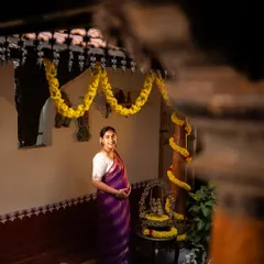 A full-length portrait of an expectant mother in a rich purple saree, standing proudly in a traditionally decorated home, embodying grace and happiness.