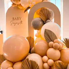 This modern baby shower setup features a Chiara wooden backdrop personalized with the baby's name. The neutral color palette with pastel balloons and dried palm leaves creates a chic and sophisticated look.