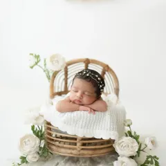 Simplicity at its best. A newborn girl rests peacefully in a cane basket, surrounded by delicate white flowers, creating a clean and classic portrait.
