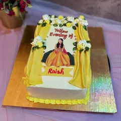 A unique cake for a "Yellow Evening" or Haldi ceremony. This rectangular cake features an edible print of the bride-to-be, framed by yellow fondant curtains and delicate flowers.
