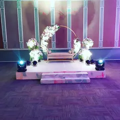 This minimalist wedding stage combines a simple wooden bench with a modern, incomplete floral arch. The clean design, paired with spotlights, creates an elegant and sophisticated focal point for the ceremony.
