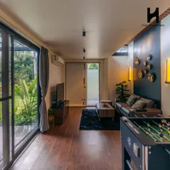 The living room of a 2BHK cargo home, featuring rich hardwood floors and a dark accent wall with gold decorative plates. The space is designed to be both stylish and comfortable, with a foosball table for entertainment.