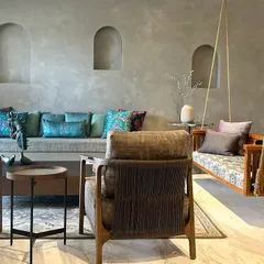 This living space is defined by its textures and tones. A concrete-finish sofa base, a traditional wooden swing, and soft woven armchairs come together to create a room that feels both contemporary and deeply rooted.